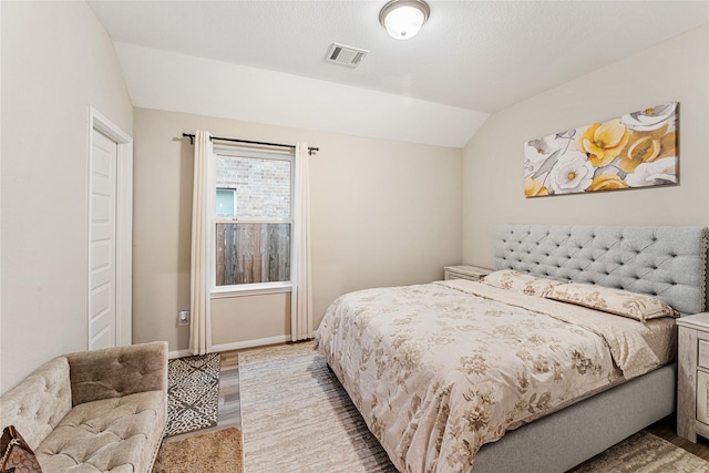 bedroom with visible vents, light wood-style flooring, a textured ceiling, baseboards, and lofted ceiling