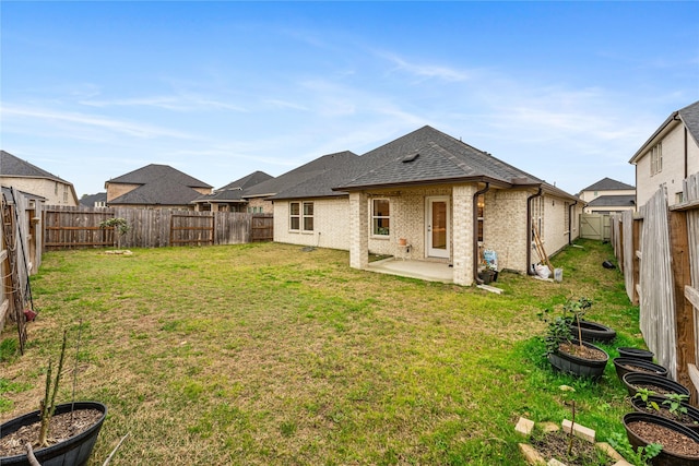 rear view of house featuring brick siding, a shingled roof, a lawn, a fenced backyard, and a patio area