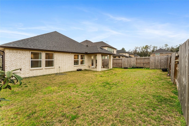 rear view of house with a lawn, a patio, a fenced backyard, a shingled roof, and brick siding