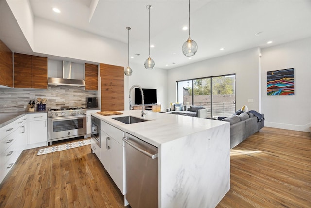 kitchen featuring a sink, tasteful backsplash, wood finished floors, stainless steel appliances, and wall chimney range hood