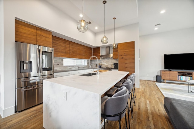 kitchen with visible vents, a sink, decorative backsplash, stainless steel refrigerator with ice dispenser, and modern cabinets