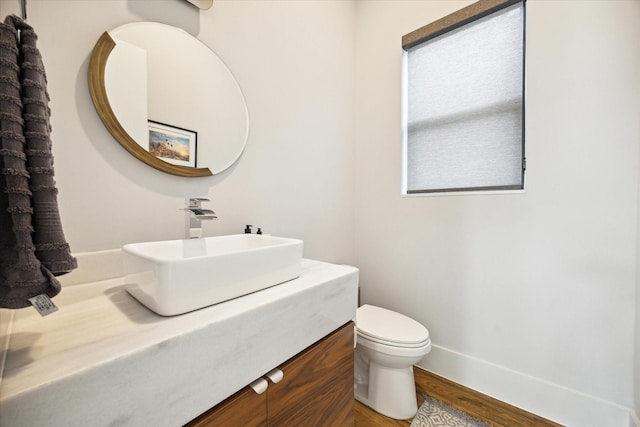 half bath with baseboards, toilet, wood finished floors, and vanity