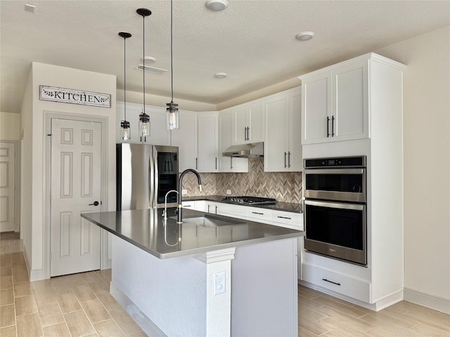 kitchen featuring under cabinet range hood, a sink, tasteful backsplash, dark countertops, and appliances with stainless steel finishes