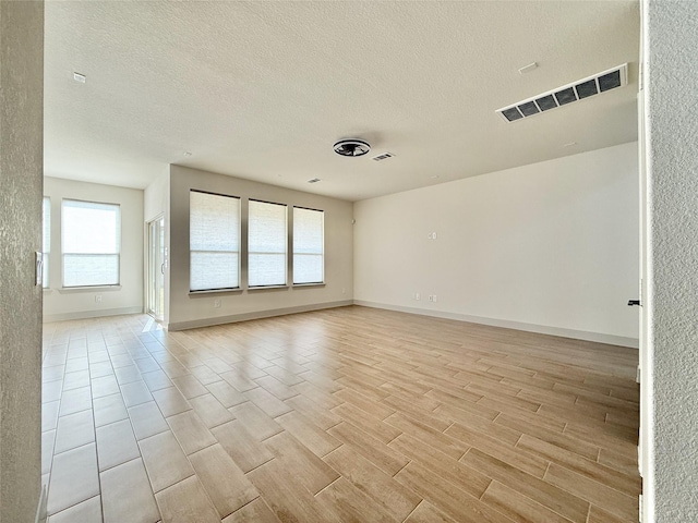 empty room with a textured ceiling, baseboards, visible vents, and light wood-type flooring