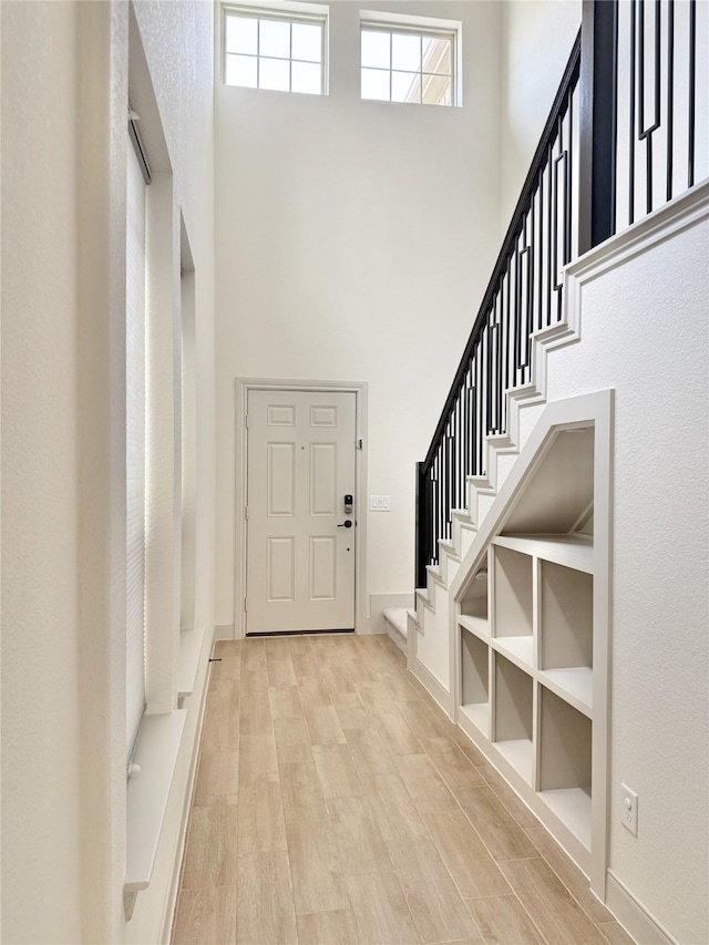 foyer with stairs, light wood-style floors, baseboards, and a towering ceiling