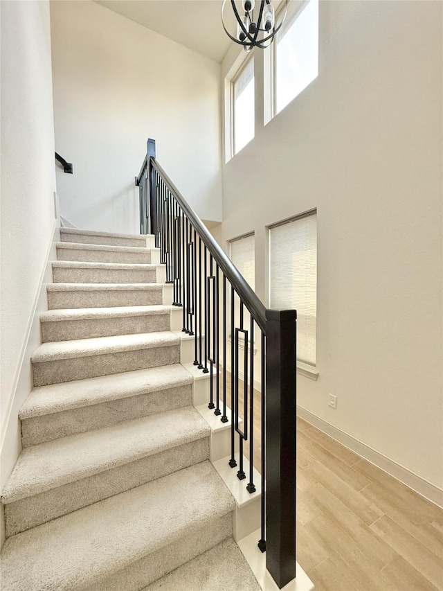 staircase with baseboards, a high ceiling, an inviting chandelier, and wood finished floors