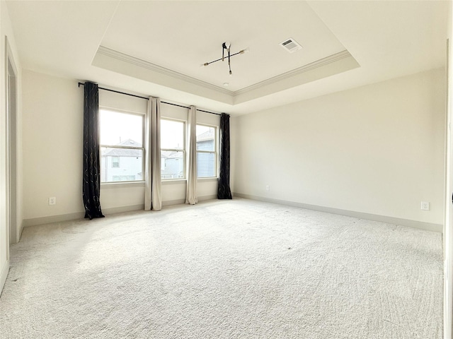 empty room featuring a tray ceiling, carpet, visible vents, and crown molding