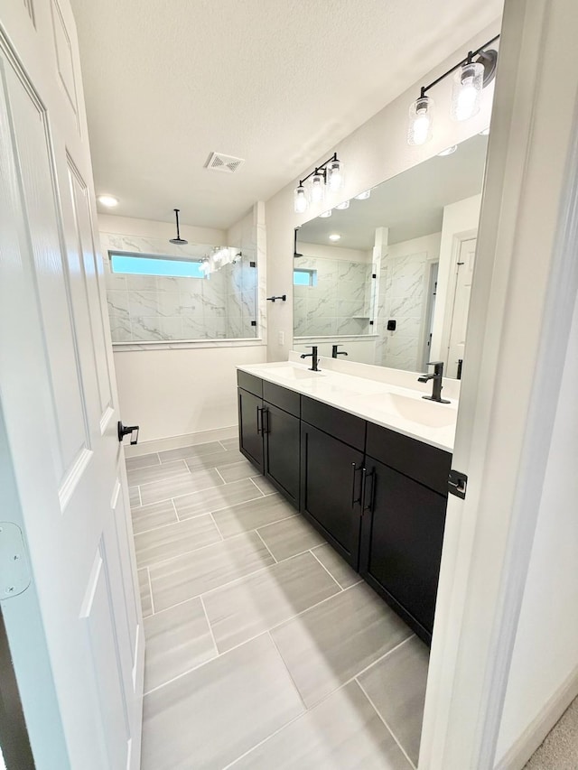 full bathroom with a textured ceiling, double vanity, a marble finish shower, and a sink