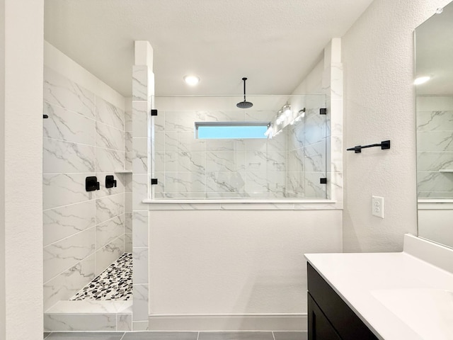 bathroom with walk in shower, vanity, and a textured wall