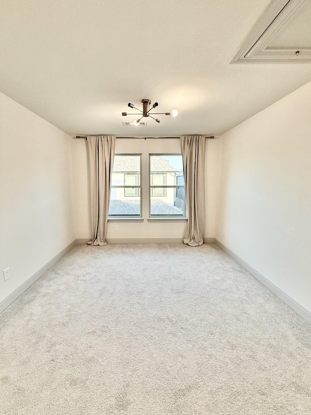 empty room with a textured ceiling, attic access, baseboards, and light carpet