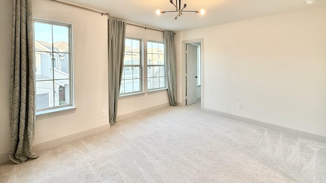 carpeted spare room featuring an inviting chandelier, a healthy amount of sunlight, and baseboards