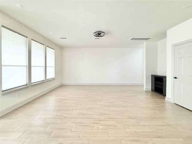 unfurnished room featuring visible vents, a textured ceiling, baseboards, and wood finish floors