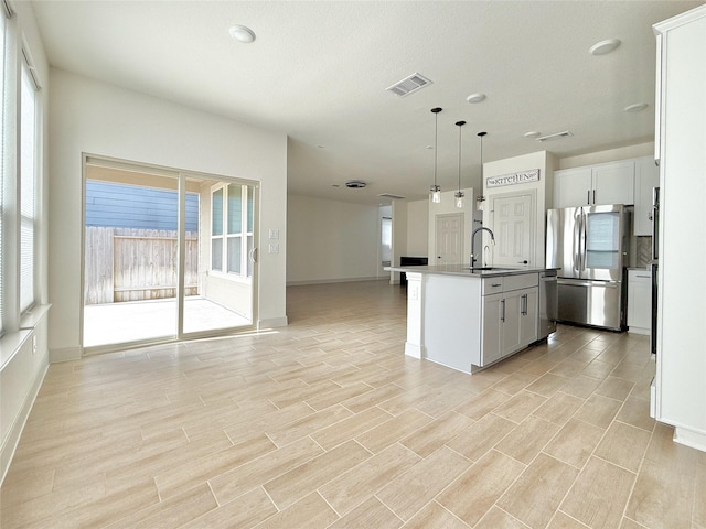 kitchen featuring open floor plan, pendant lighting, an island with sink, appliances with stainless steel finishes, and a sink