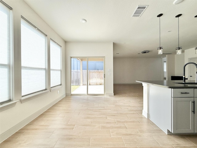 kitchen with dark countertops, visible vents, decorative light fixtures, open floor plan, and a sink