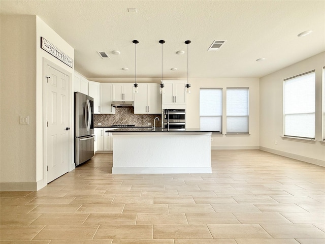 kitchen with visible vents, under cabinet range hood, appliances with stainless steel finishes, dark countertops, and backsplash