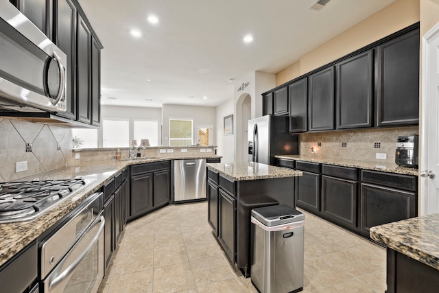 kitchen featuring decorative backsplash, light stone countertops, appliances with stainless steel finishes, and dark cabinets