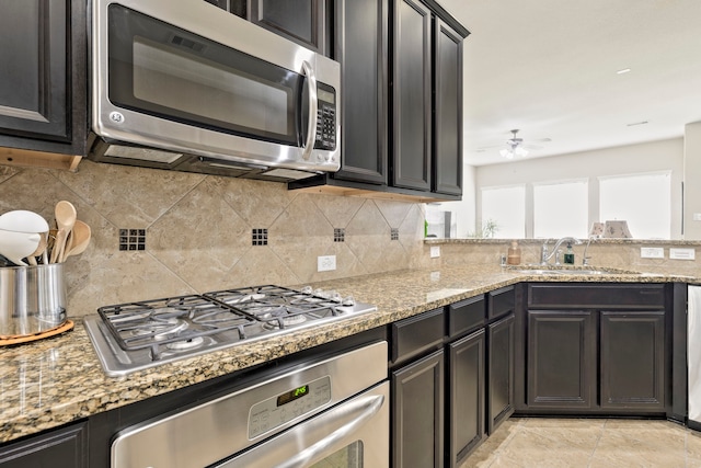 kitchen with a ceiling fan, a sink, light stone counters, appliances with stainless steel finishes, and decorative backsplash