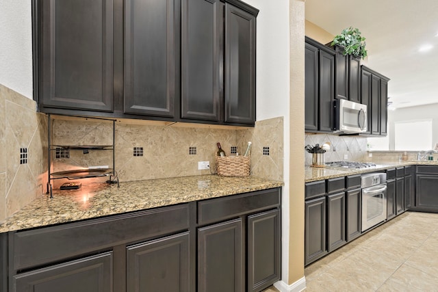 kitchen featuring tasteful backsplash, light stone countertops, appliances with stainless steel finishes, light tile patterned flooring, and a sink