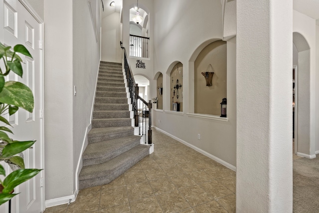 stairs featuring baseboards, a towering ceiling, and tile patterned flooring