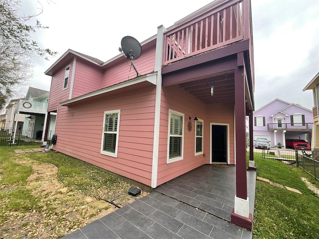 rear view of house with a yard, fence, a balcony, and a patio area