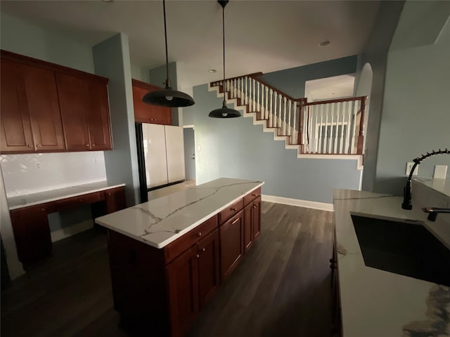 kitchen with light stone countertops, a kitchen island, dark wood-style flooring, a sink, and hanging light fixtures