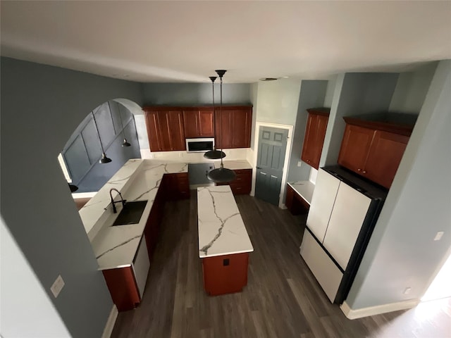 kitchen featuring a sink, stainless steel microwave, light stone counters, decorative light fixtures, and dark wood finished floors