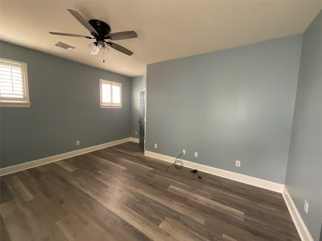 empty room featuring ceiling fan, visible vents, baseboards, and dark wood finished floors