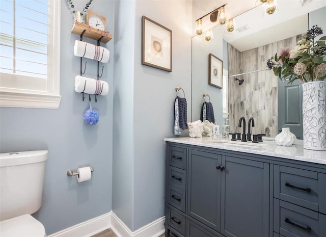 bathroom with baseboards, toilet, vanity, and a tile shower