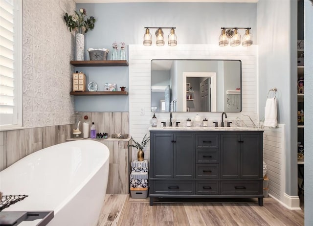 bathroom featuring a sink, wood finished floors, tile walls, double vanity, and a freestanding bath