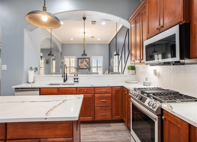 kitchen with pendant lighting, ornamental molding, a sink, light stone counters, and stainless steel appliances