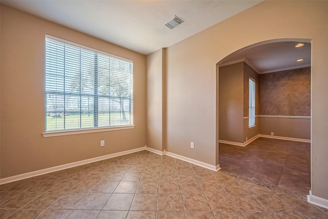 spare room featuring arched walkways, tile patterned floors, and baseboards