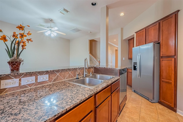 kitchen featuring stainless steel fridge, a sink, brown cabinetry, a ceiling fan, and stone counters