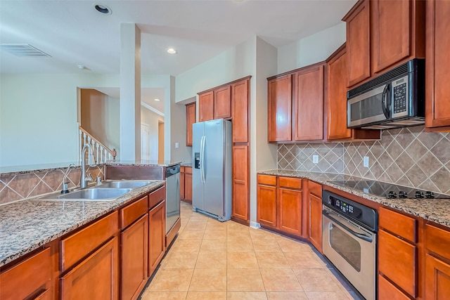 kitchen featuring appliances with stainless steel finishes, a sink, brown cabinetry, backsplash, and stone countertops