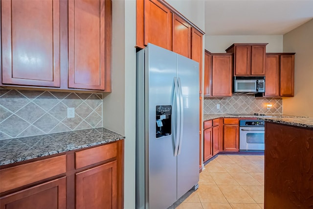 kitchen with black appliances, tasteful backsplash, dark stone counters, brown cabinetry, and light tile patterned flooring