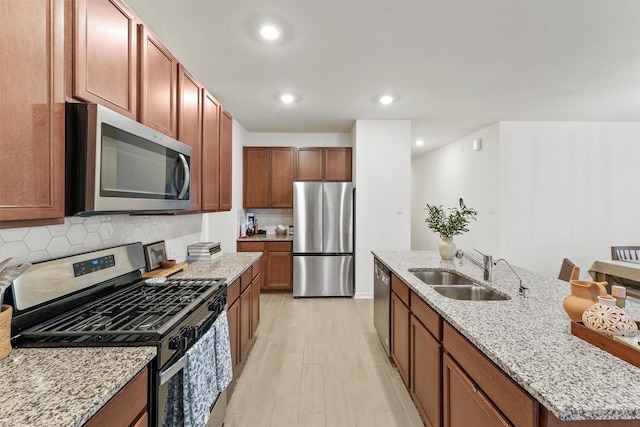 kitchen featuring an island with sink, a sink, backsplash, stainless steel appliances, and light stone countertops