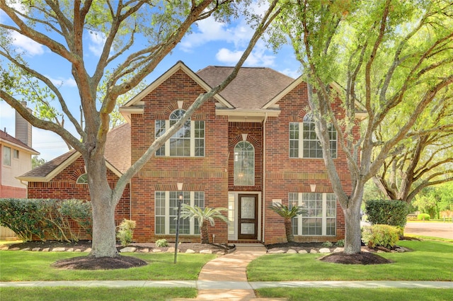 traditional home featuring a front lawn, brick siding, and a shingled roof