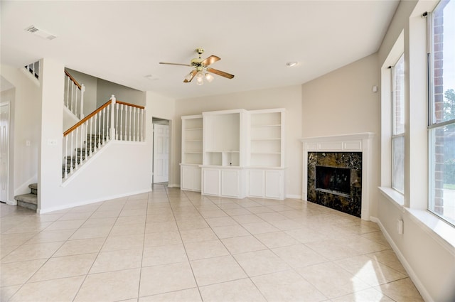 unfurnished living room featuring visible vents, a ceiling fan, a healthy amount of sunlight, a fireplace, and stairs