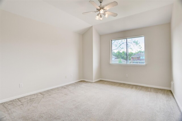 carpeted spare room with vaulted ceiling, a ceiling fan, and baseboards
