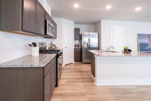 kitchen with tasteful backsplash, dark brown cabinetry, light wood-style flooring, appliances with stainless steel finishes, and a sink