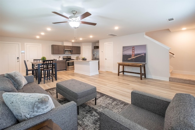 living room featuring visible vents, light wood-style flooring, a ceiling fan, and stairway