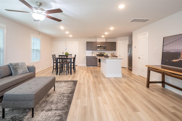 living room featuring light wood-type flooring, visible vents, a ceiling fan, recessed lighting, and baseboards