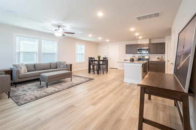 living area featuring visible vents, light wood-style flooring, a ceiling fan, recessed lighting, and baseboards