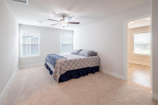 carpeted bedroom featuring visible vents, multiple windows, a ceiling fan, and baseboards