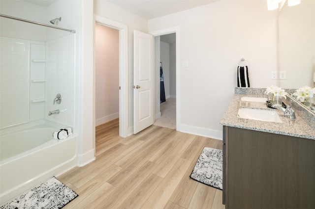 full bath featuring baseboards, shower / washtub combination, double vanity, wood finished floors, and a sink