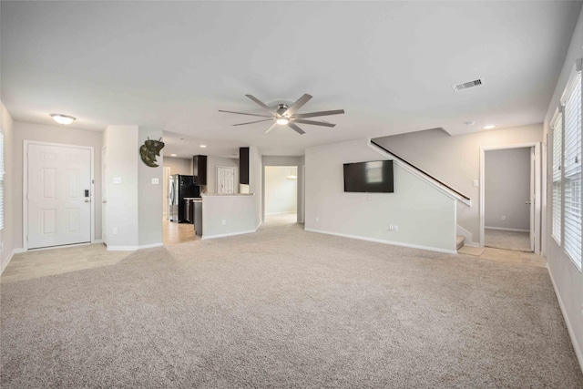 unfurnished living room with baseboards, visible vents, ceiling fan, stairs, and light colored carpet