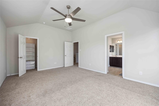 unfurnished bedroom with light carpet, baseboards, ensuite bath, and lofted ceiling