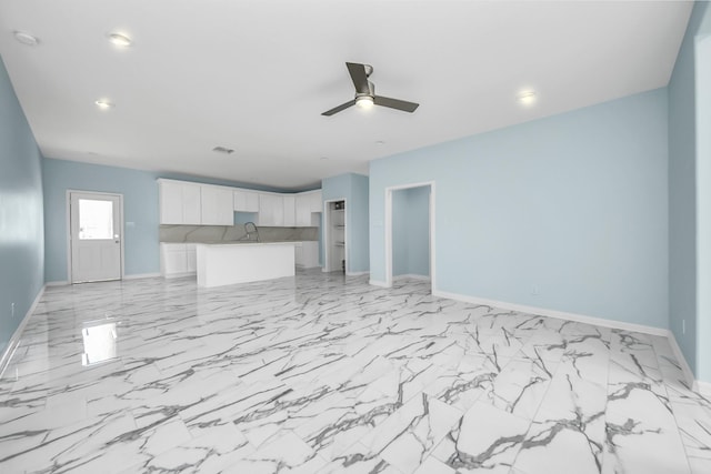 unfurnished living room featuring marble finish floor, baseboards, ceiling fan, and a sink