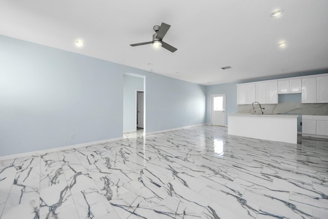 unfurnished living room with a sink, visible vents, baseboards, and ceiling fan