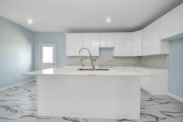 kitchen with baseboards, a center island with sink, marble finish floor, white cabinetry, and a sink