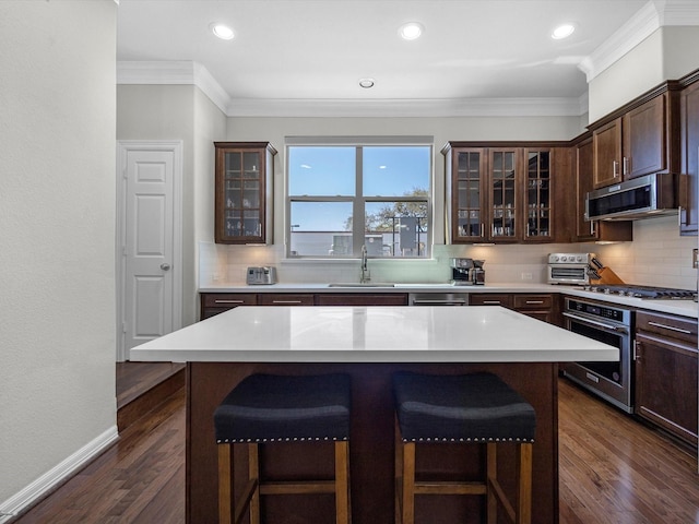 kitchen with backsplash, dark brown cabinetry, a breakfast bar, appliances with stainless steel finishes, and a sink